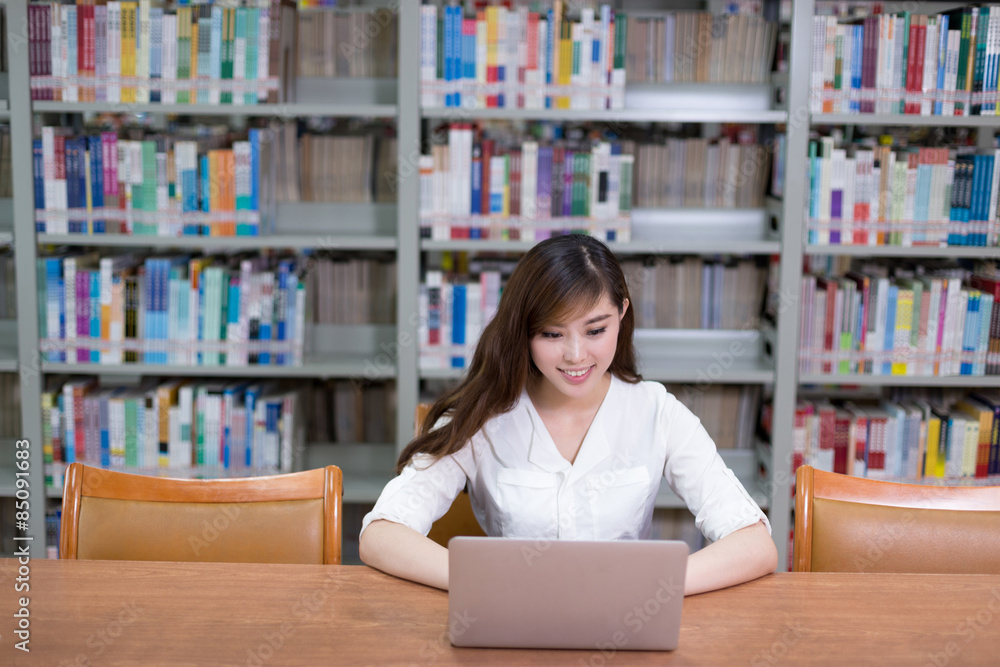 漂亮的亚洲女学生在图书馆用笔记本电脑学习