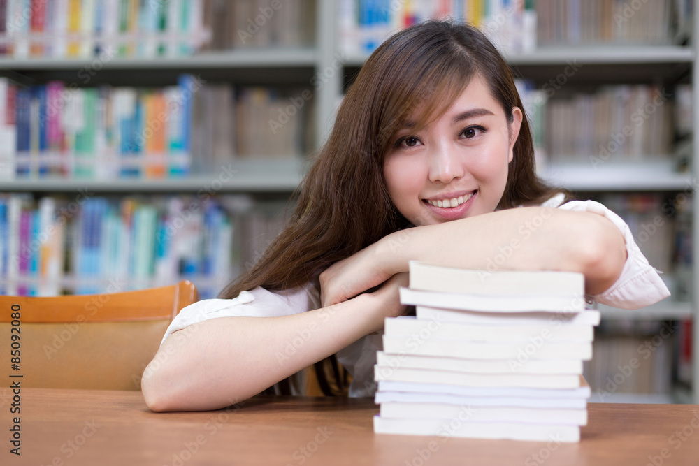 美丽的亚洲女学生肖像和图书馆智慧中的书籍