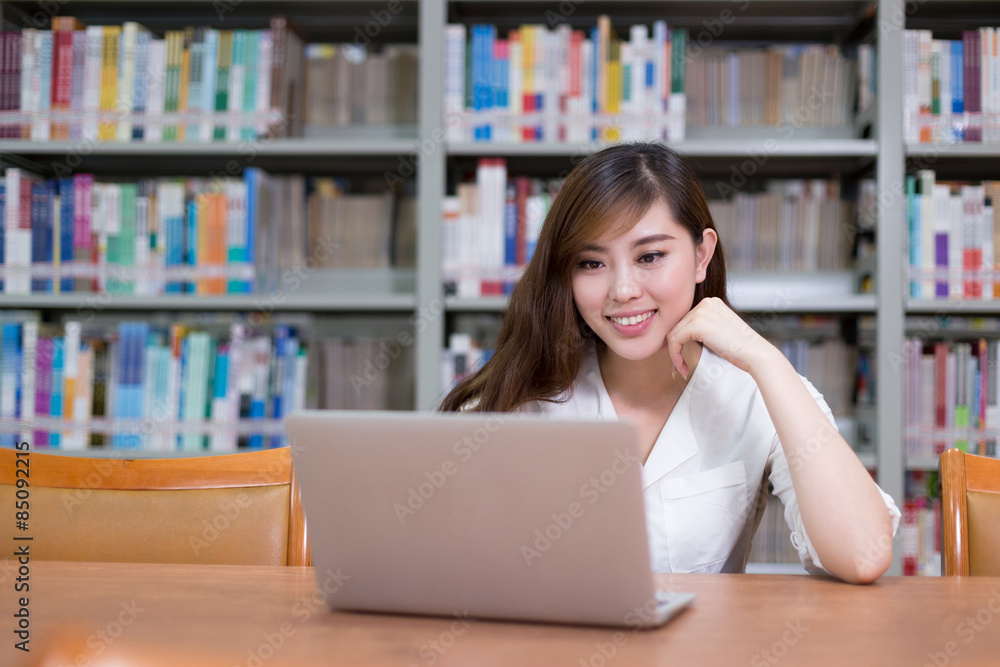 漂亮的亚洲女学生在图书馆用笔记本电脑学习