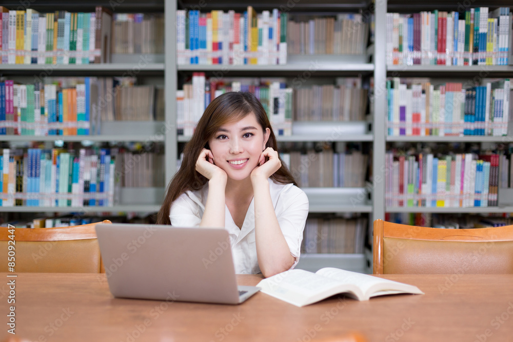 美丽的亚洲女学生在图书馆使用笔记本电脑学习