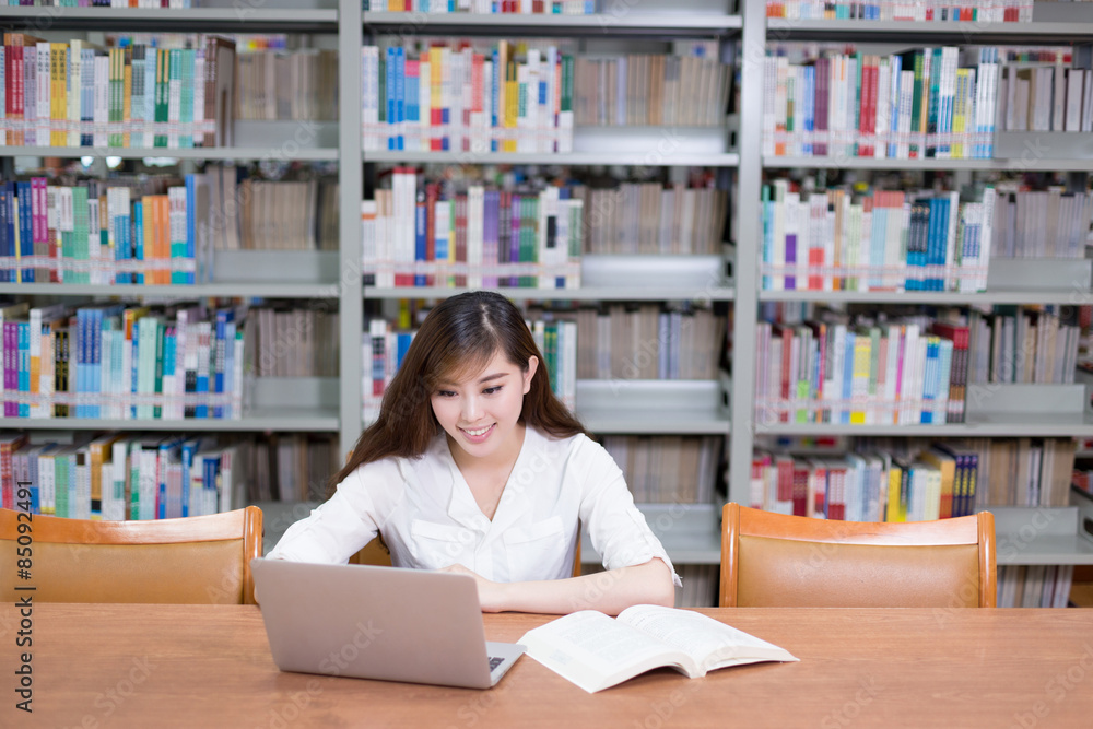 漂亮的亚洲女学生在图书馆用笔记本电脑学习