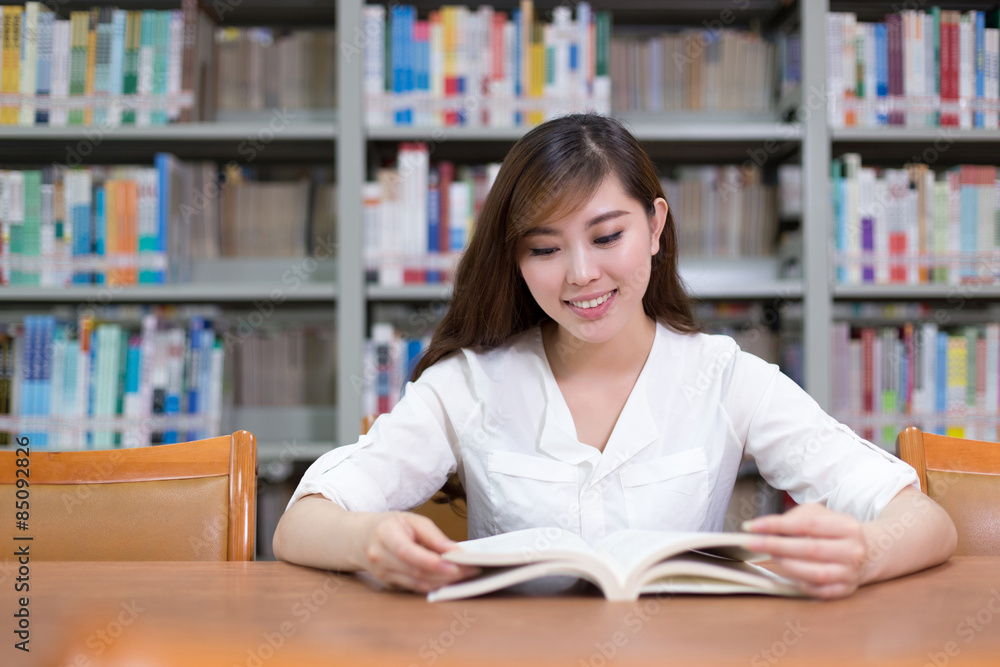 美丽的亚洲女学生在图书馆看书