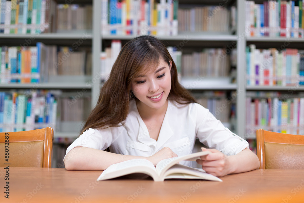 美丽的亚洲女学生在图书馆看书