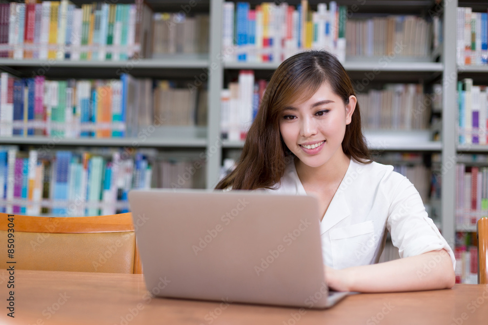 漂亮的亚洲女学生在图书馆用笔记本电脑学习