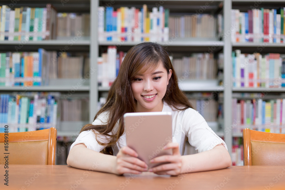 漂亮的亚洲女学生在图书馆使用数字平板电脑