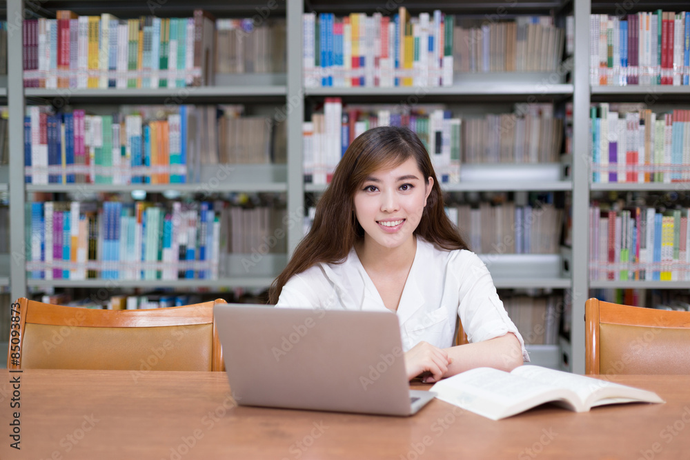 漂亮的亚洲女学生在图书馆用笔记本电脑学习