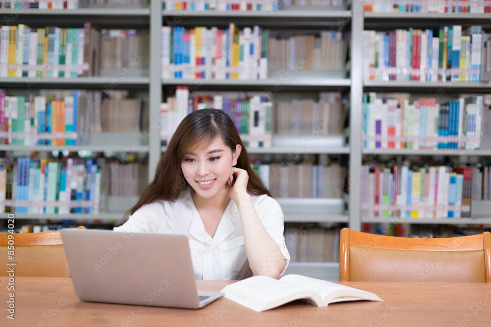 漂亮的亚洲女学生在图书馆用笔记本电脑学习