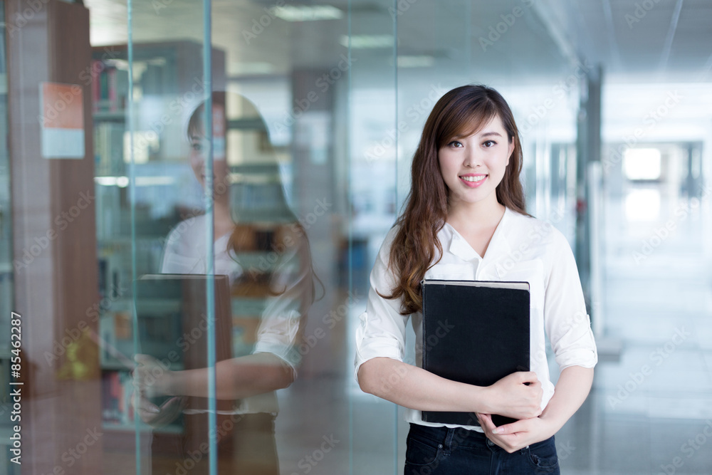 Asian beautiful female student holding book in library