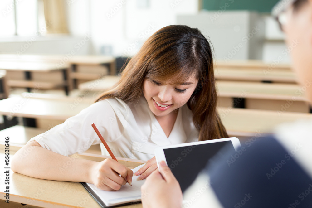 两名亚洲学生在课堂上讨论平板电脑上的内容