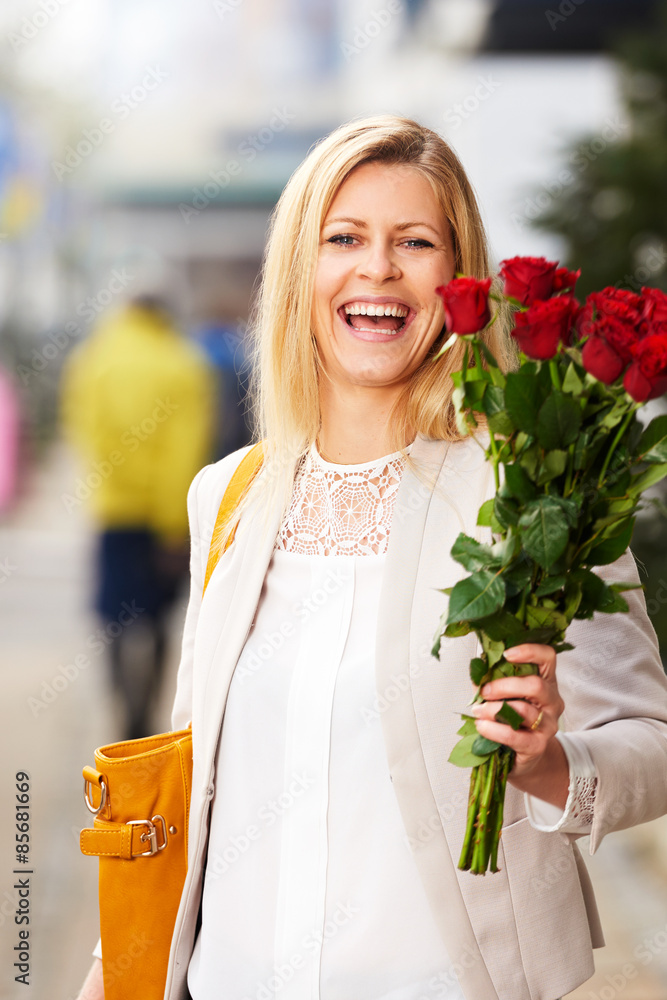 Laughing woman posing on sidewalk holding red roses