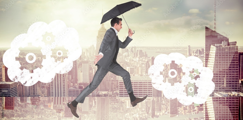 Composite image of businessman jumping holding an umbrella