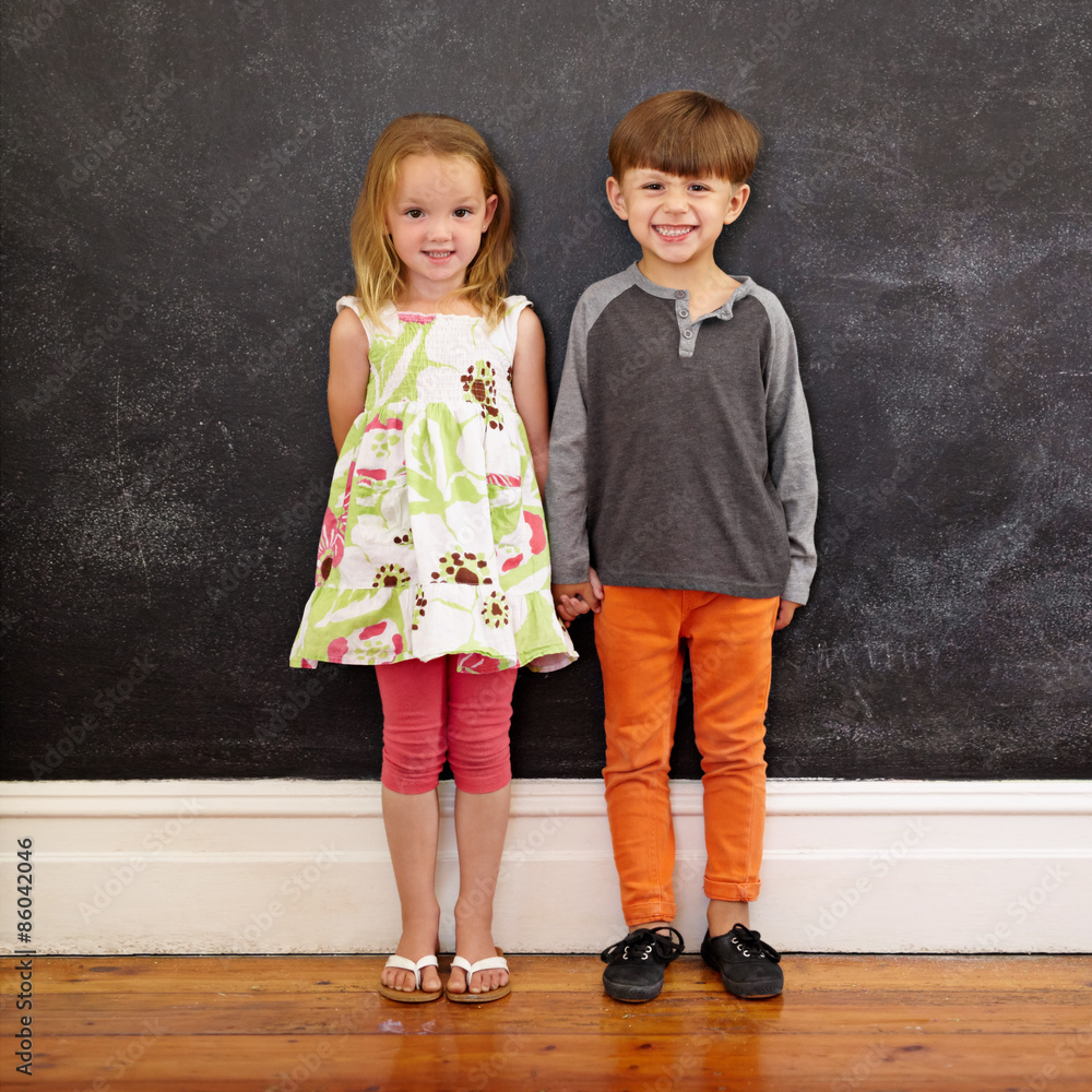 Two little kids standing together against blackboard