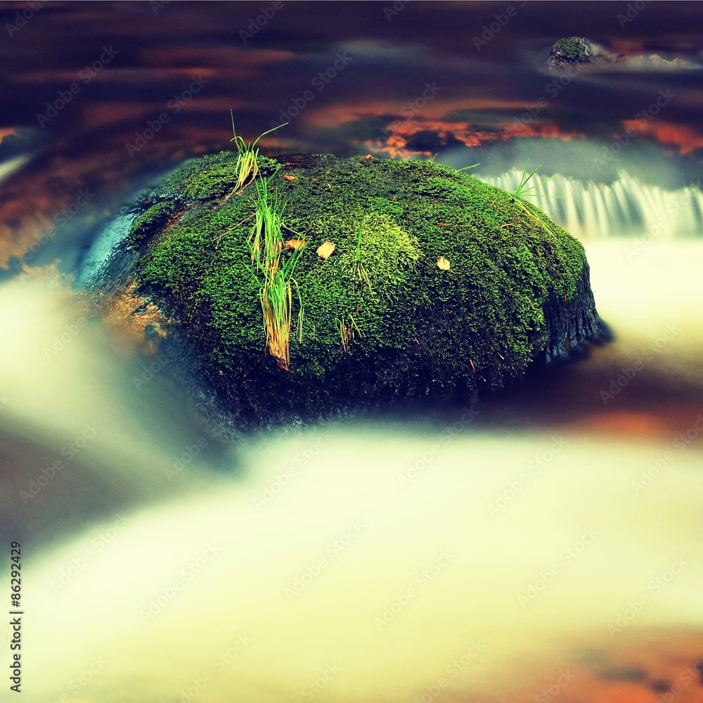 Big boulders covered by fresh green moss in foamy water of mountain river. Light blurred cold water 