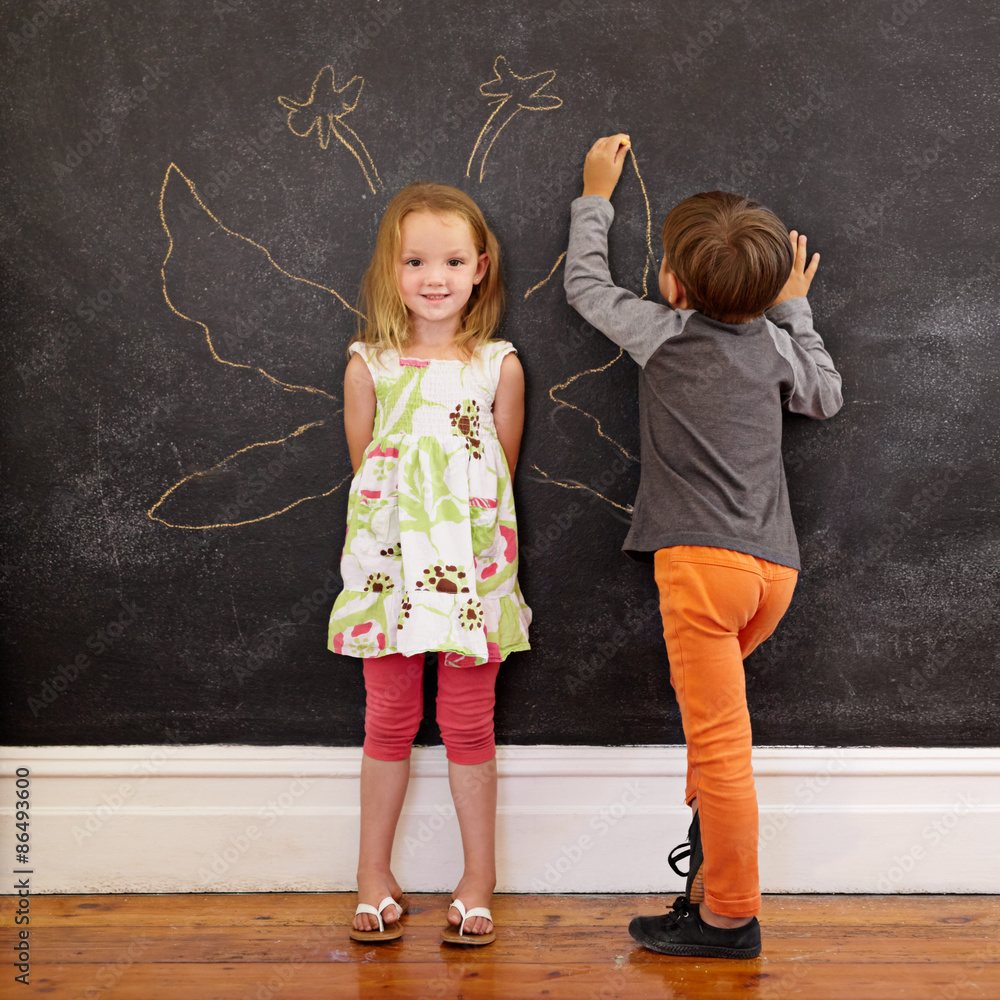 Little girl in front of a blackboard with boy drawing angel wing