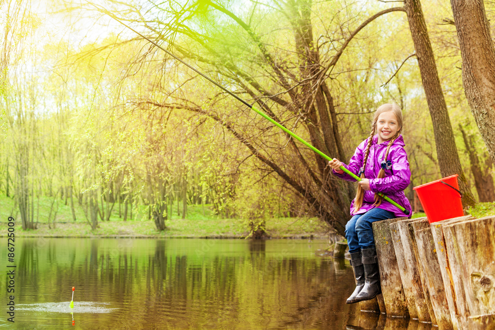 Smiling small girl fishing near beautiful pond