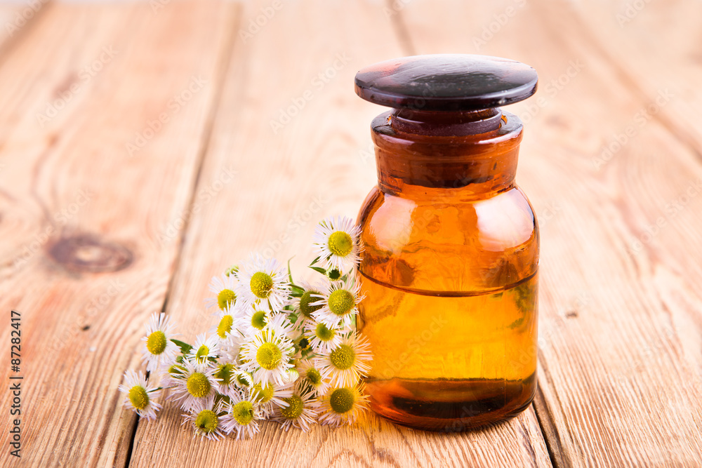 fragrant oil in a glass bottle with camomile flowers on wooden t