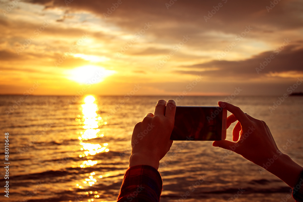 hands holding mobile phone at sunset