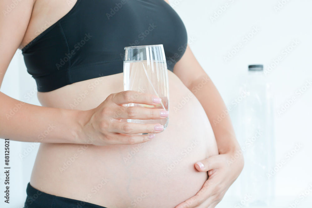 Healthy mother to be holding a glass of water in front of her belly