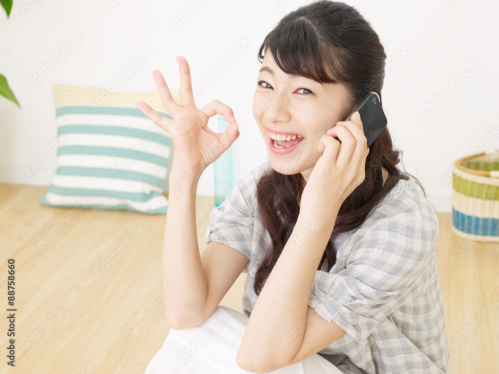 スマホで話しながらOKサインする女性