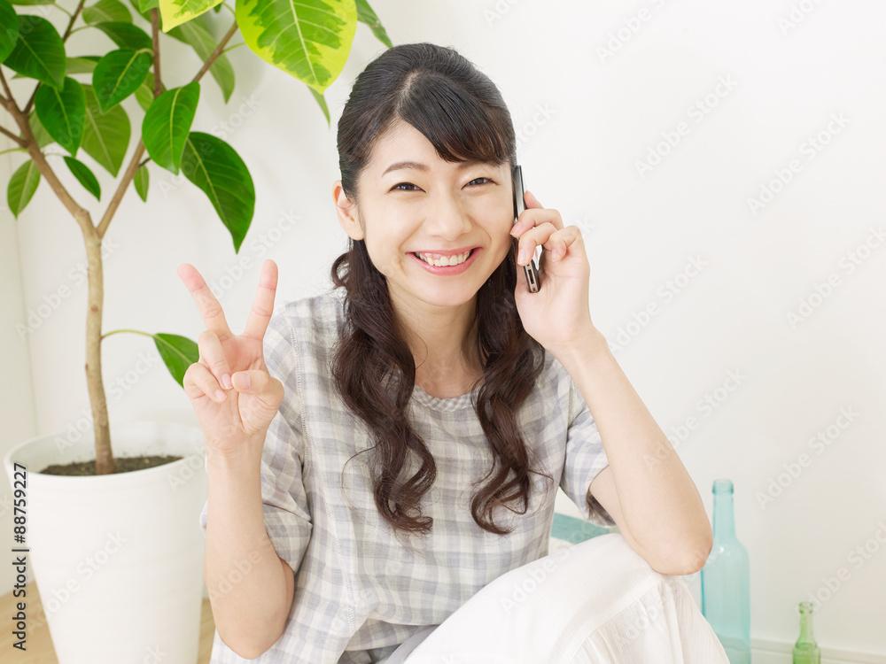 スマホで話しながらピースサインする女性