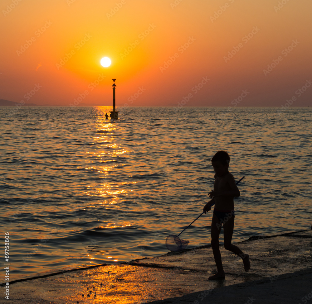 Cute boy playing with landing net  on the beach. Amazing sunset