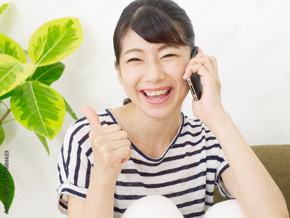 部屋でスマートフォンで話す女性　グッドサイン