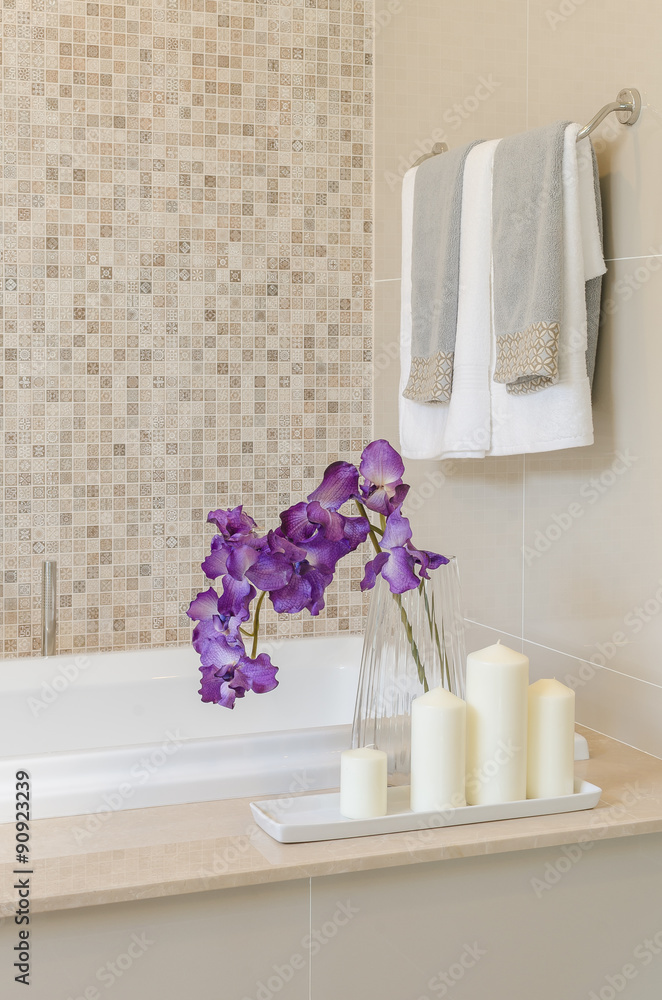 glass vase of flower on bath tub with towel hanging