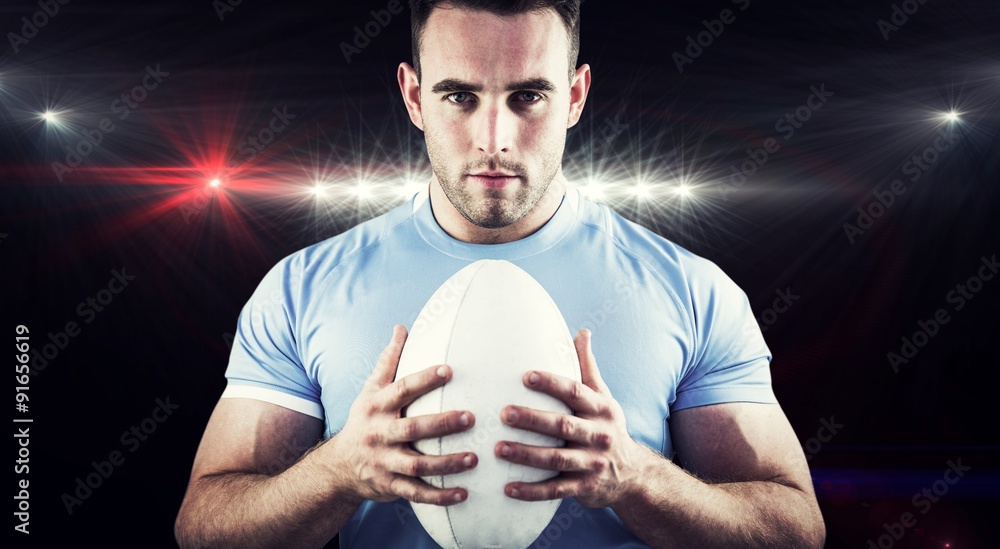 Composite image of rugby player looking at camera with ball