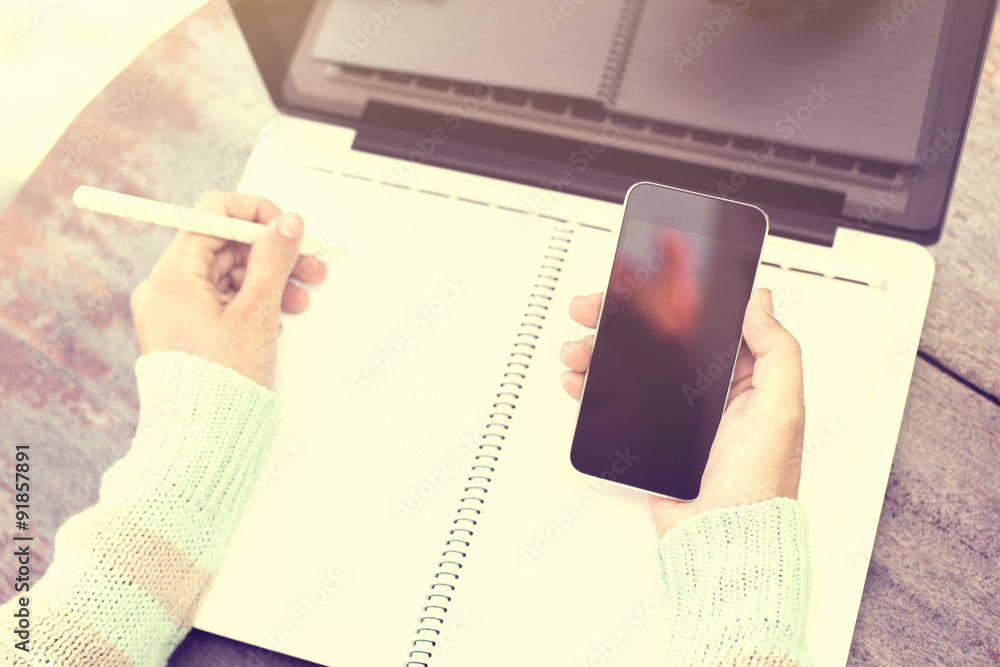 girl writing in a notebook with a cell phone and a laptop