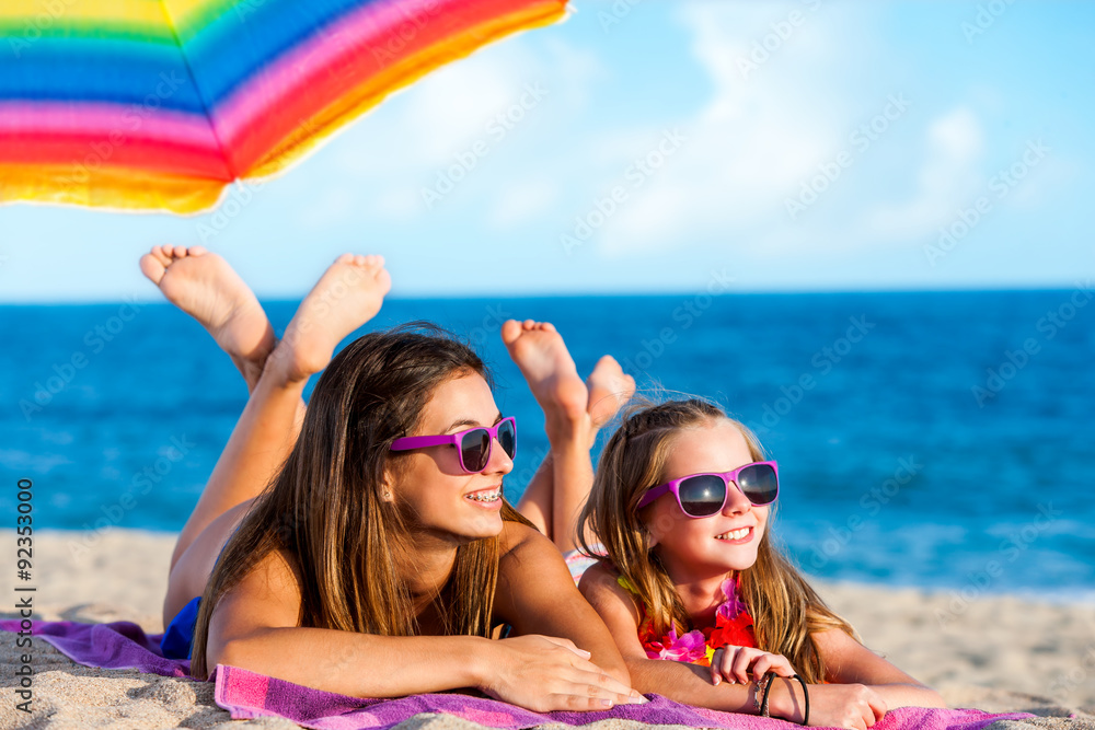 Two young girls wearing fun purple sunglasses laying together on beach.