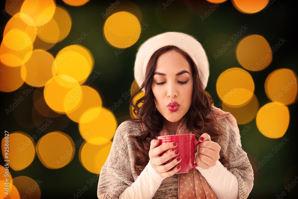 Composite image of brunette in winter clothes holding hot drink 