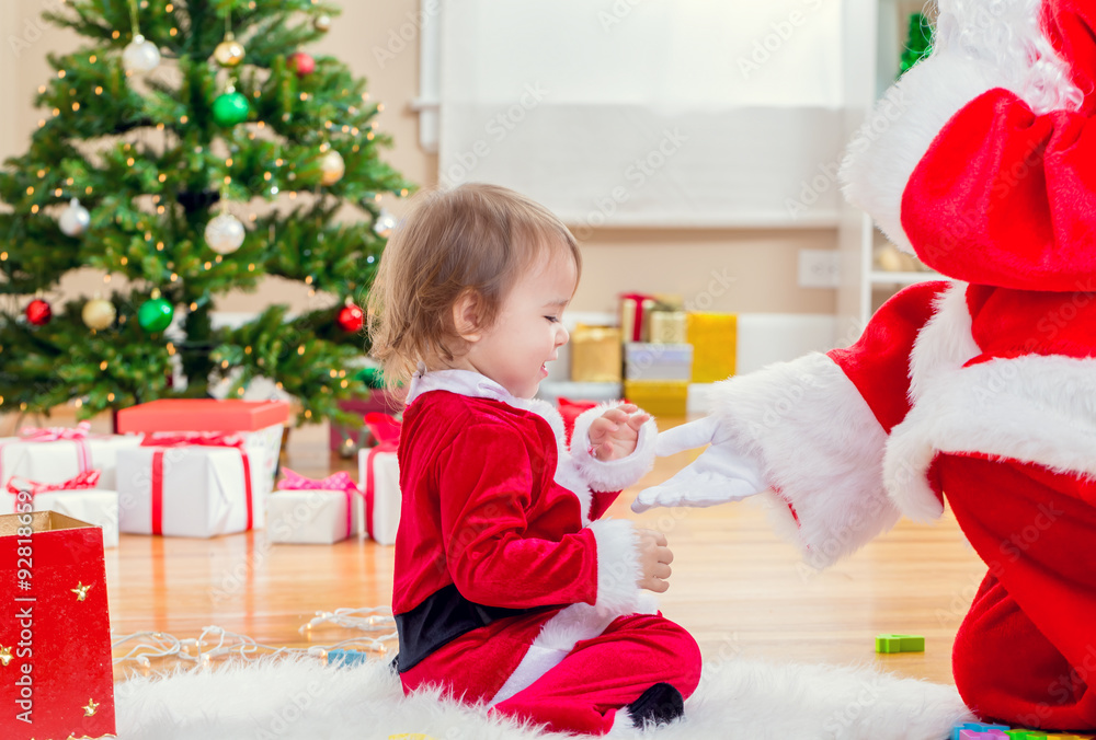 Little girl interacting with Santa Claus by the Christmas tree