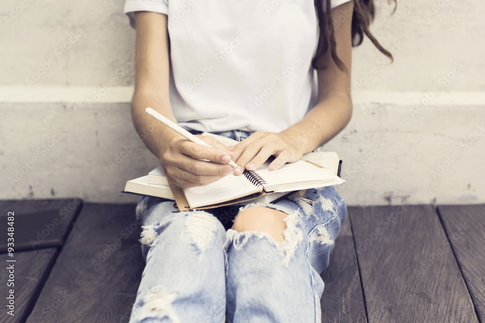 Girl making notes in the diary and sitting on a wooden floor