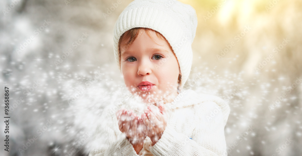 happy child girl blowing snowflakes in winter outdoors