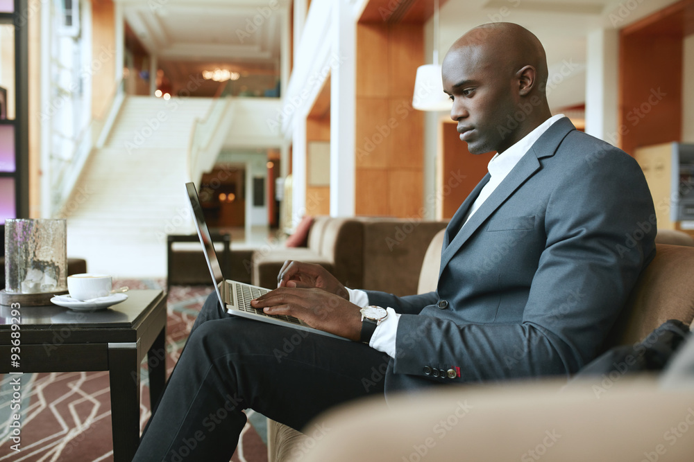 Busy young businessman working on laptop in lobby