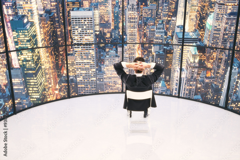 Businessman looking to the city at evening in an empty white roo