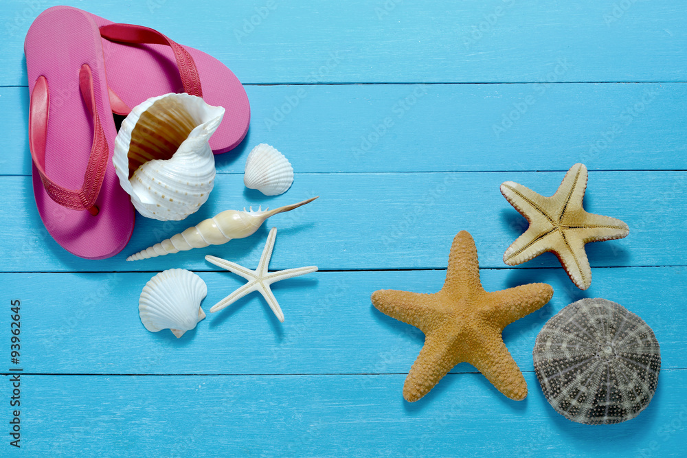 Flip flops with starfish and seashells on wooden background