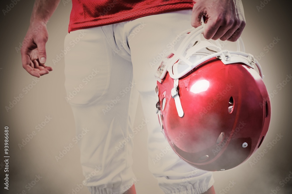 An american football player taking his helmet on her hand  against grey background with vignette