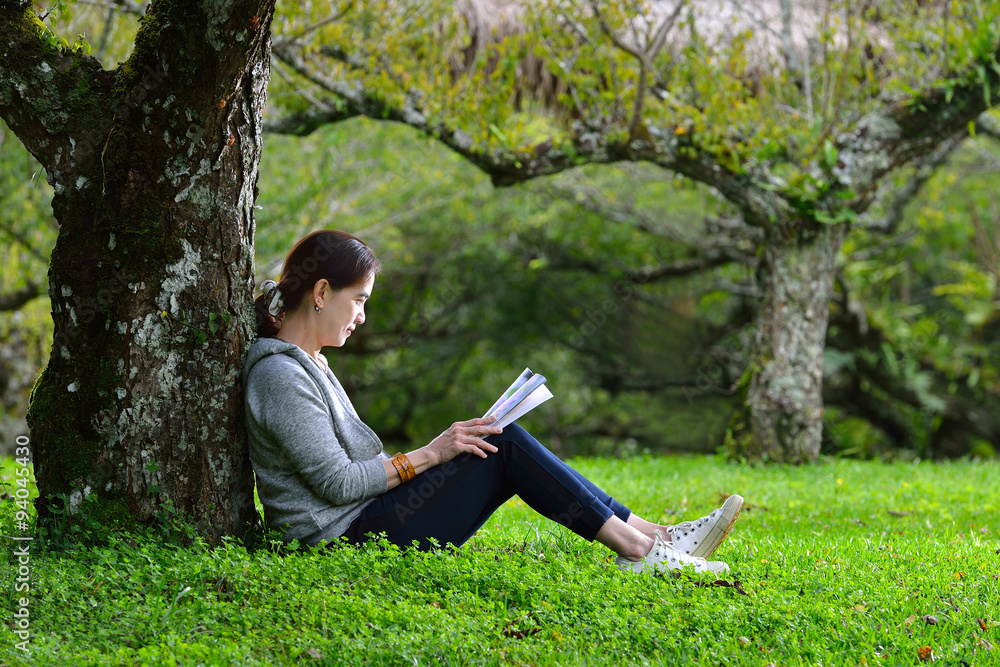 Middle aged woman sitting under a tree reading a book