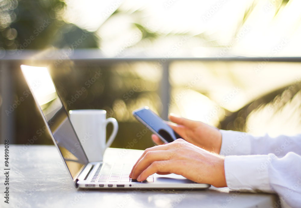 Man hand with laptop and smartphone outdoor at sunrise