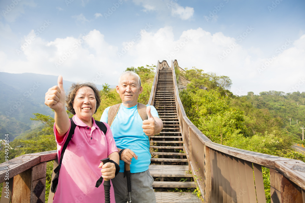 happy  senior couple hiking on the mountain with thumbs up