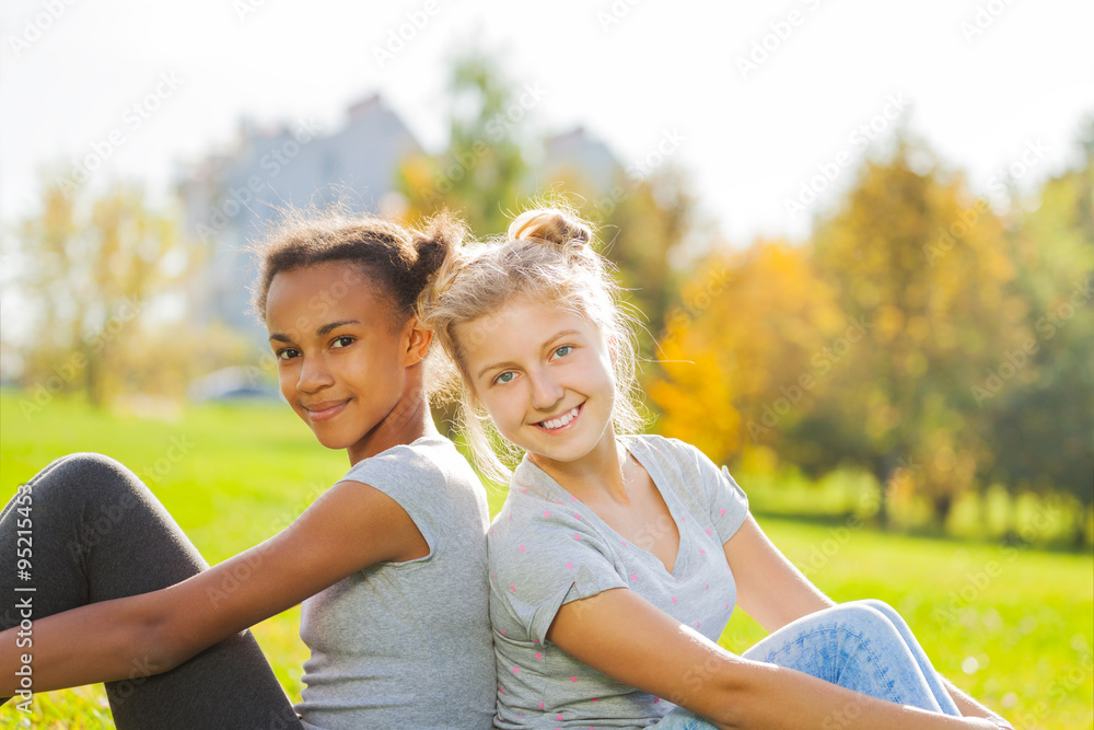 African and blond girl sitting together in park