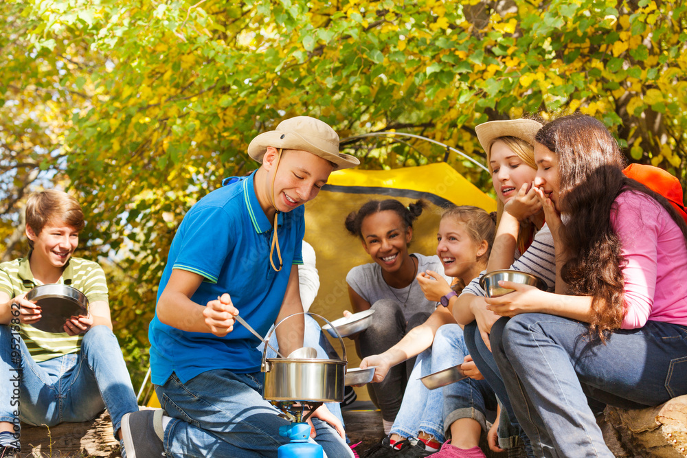 Boy cooks soup in pot for friends at campsite