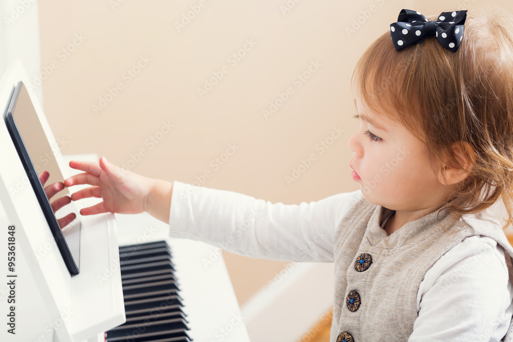 Toddler girl playing the piano with help from her tablet