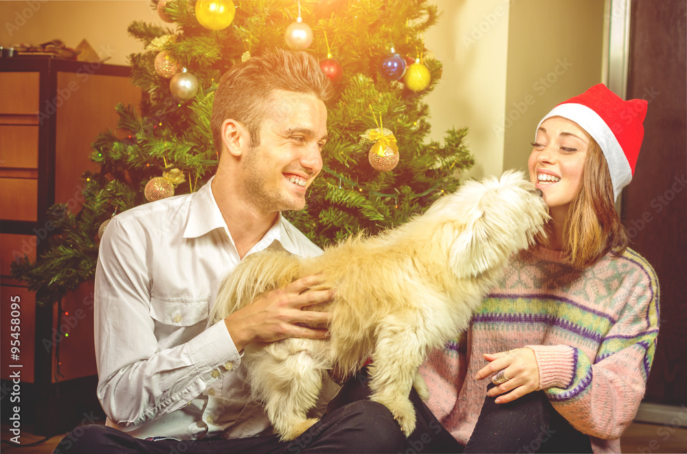 Merry Christmas and Happy New Year. Young beautiful couple are playing with their dog  in festive Ne