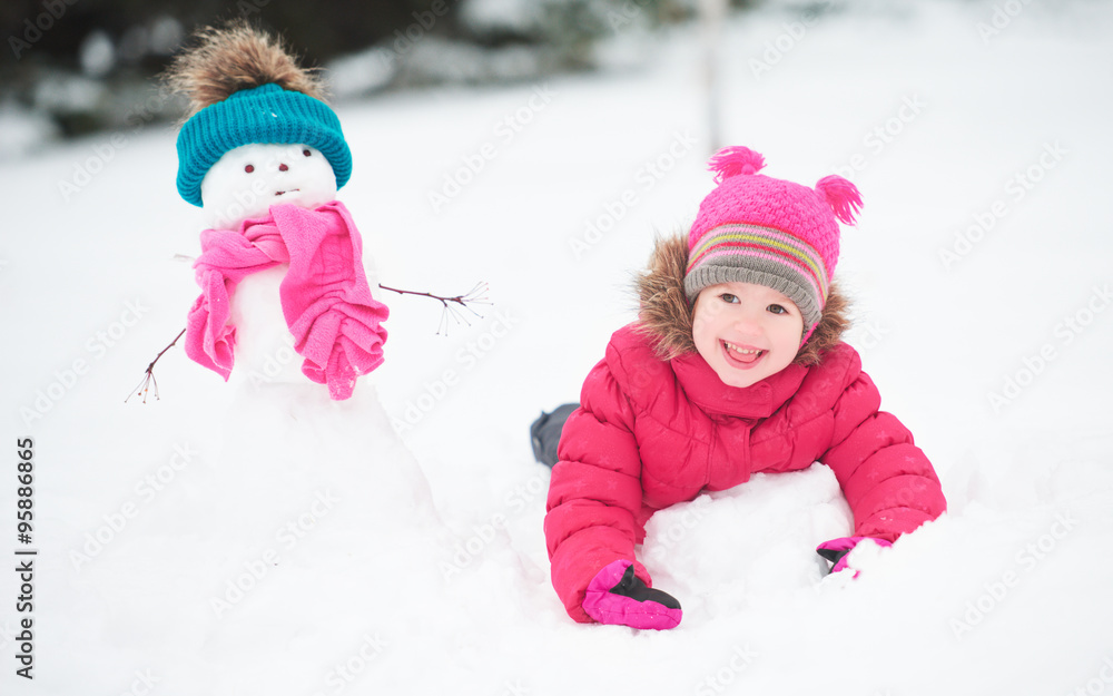 happy child girl with a snowman on a winter walk