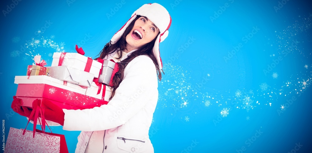 Composite image of brunette in winter clothes holding gifts