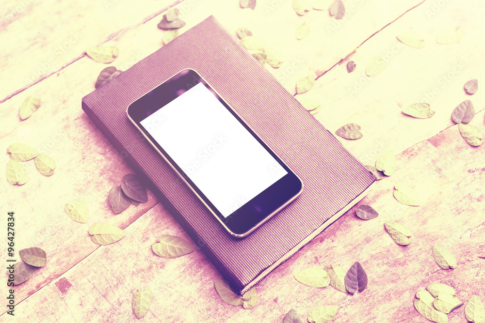 Blank white screen smartphone with diary on wooden table with le