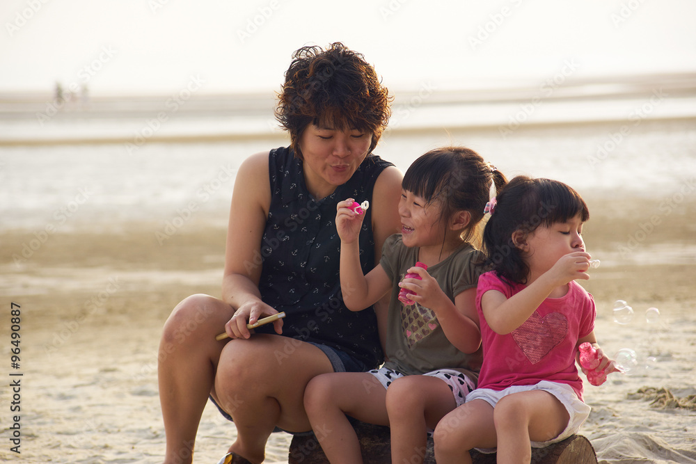 年轻的妈妈和两个快乐的孩子一起做肥皂泡