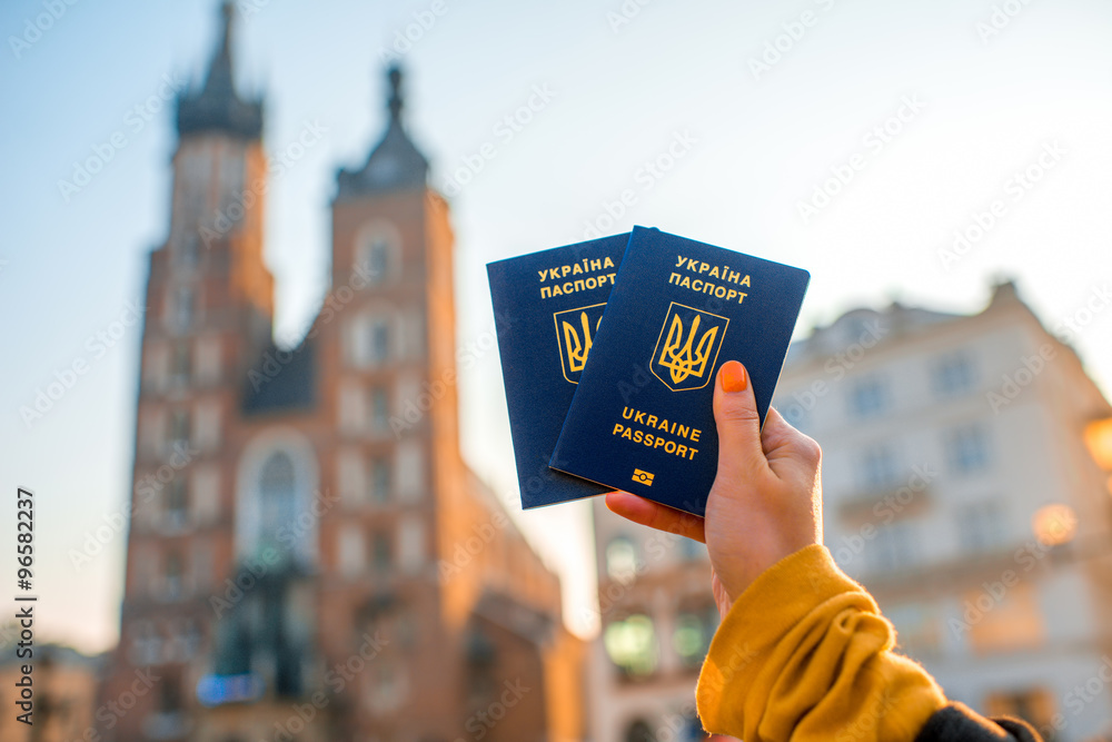 Female hands holding Ukrainian abroad passports on the Krakow city center background